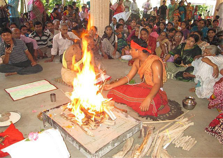 A young man performing a fire ritual while an old man reciting some scriptures
