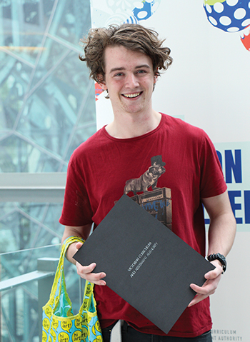 A young man wearing a red tshirt smiling and holding a certificate