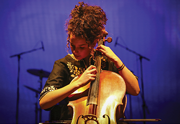 a young woman with long curly broan hair looking down at her cello while she plays it