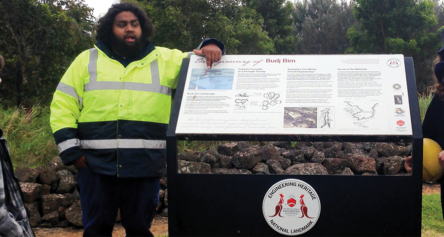 An Aboriginal man standing near a sign for Budj Bim talking to a tour group