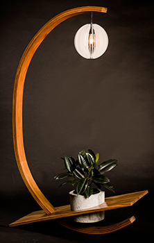 a large thin crescent shape made of wood, a light in a round shade hangs from the top of the crescent