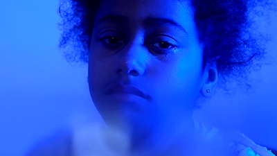 a young woman looks at the camera in a black and blue duotone image still from the film Hereafter