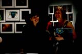 Two women smile in an exhibition space with photographs on wall behind
