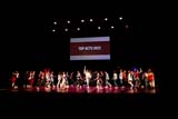 Thirty-one young people dance around a stage. Behind them a screen reads TOP ACTS 2022.