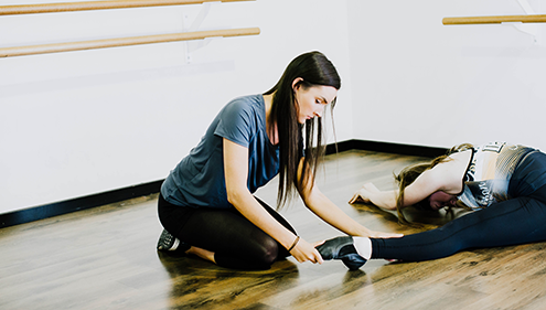 A female VET Dance student helping another student doing leg stretches